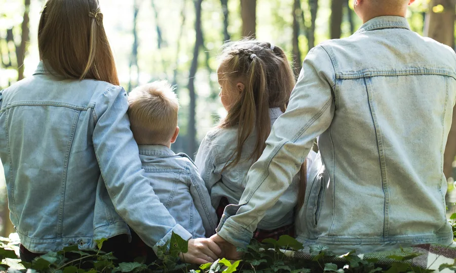 Una familia sentada de espaldas al aire libre, abrazada, mirando los árboles