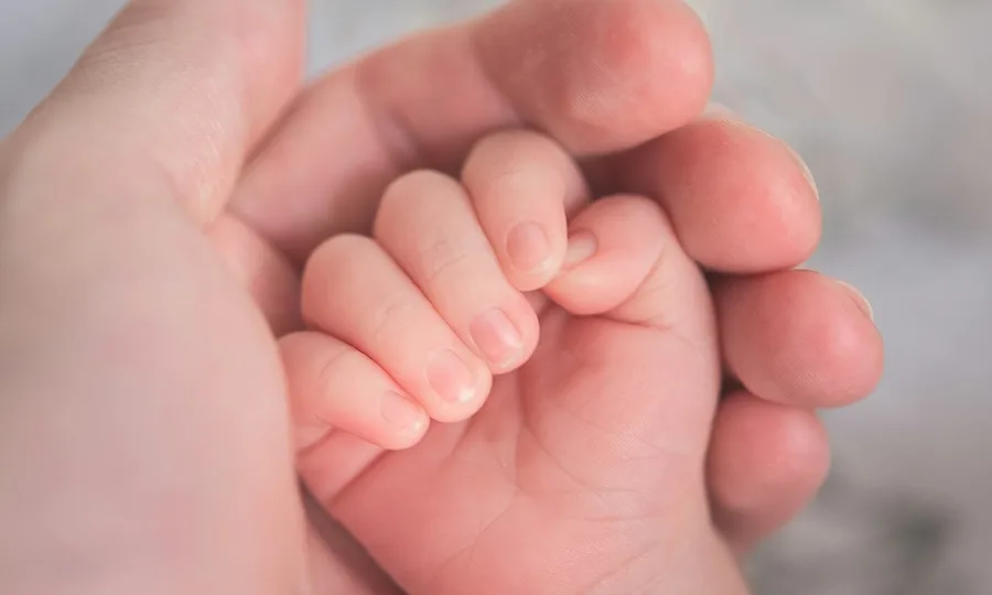 La mano de un adulto sosteniendo con cuidado la mano de un bebé